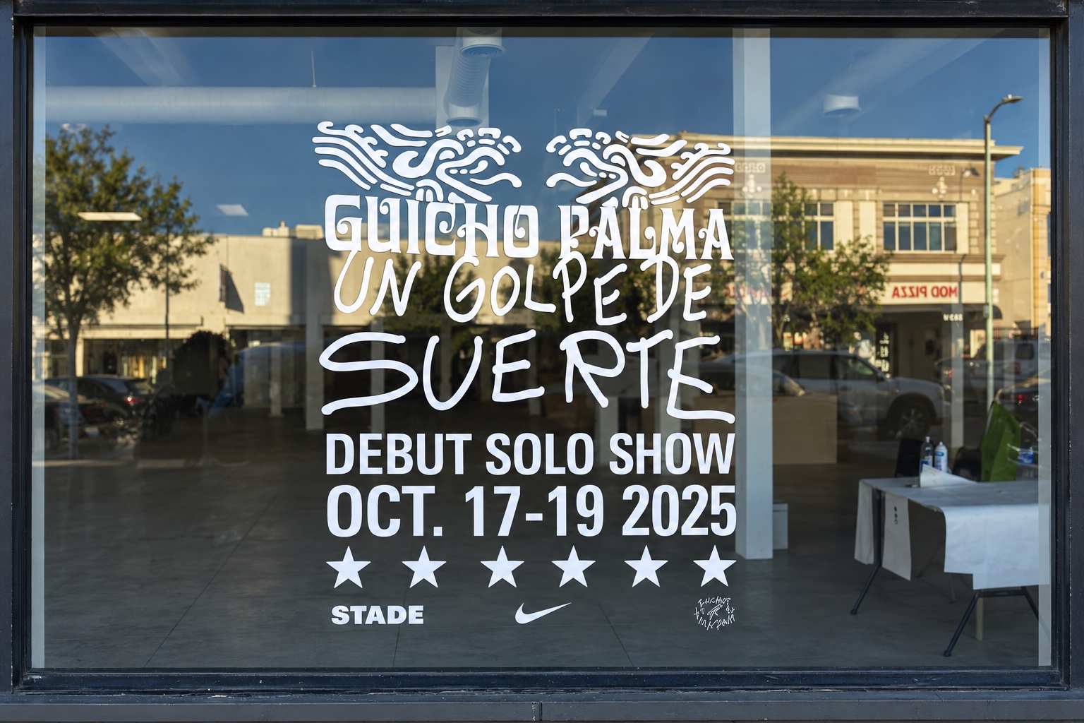 Straight-on view of Guicho Palma exhibition lettering installed across a storefront window