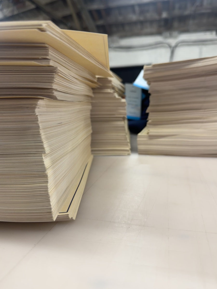 Stacks of cream Hey Janice event invitations during production